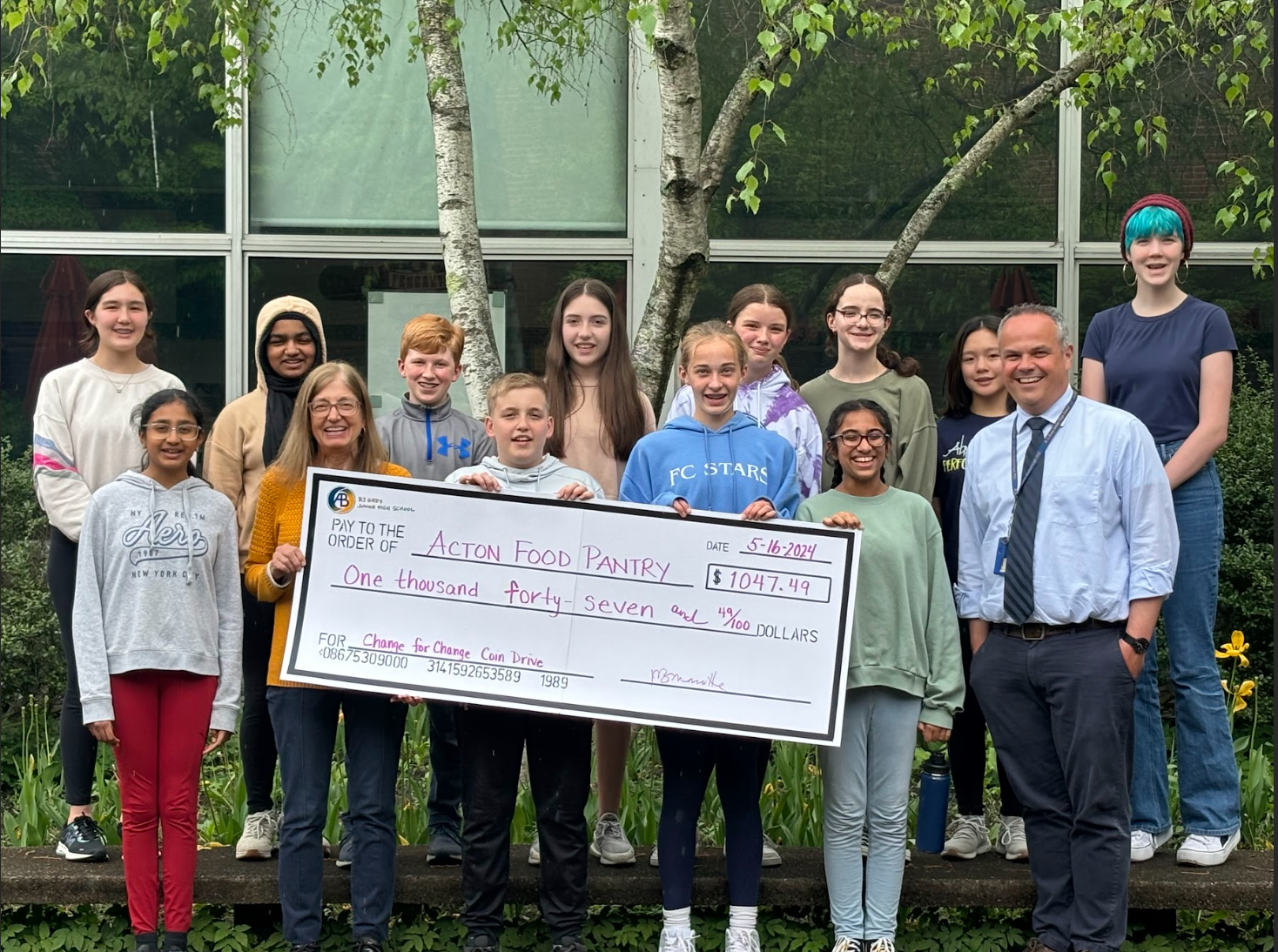 A group of 7th grade students present an oversize check for the Acton Food Pantry to a smiling woman.