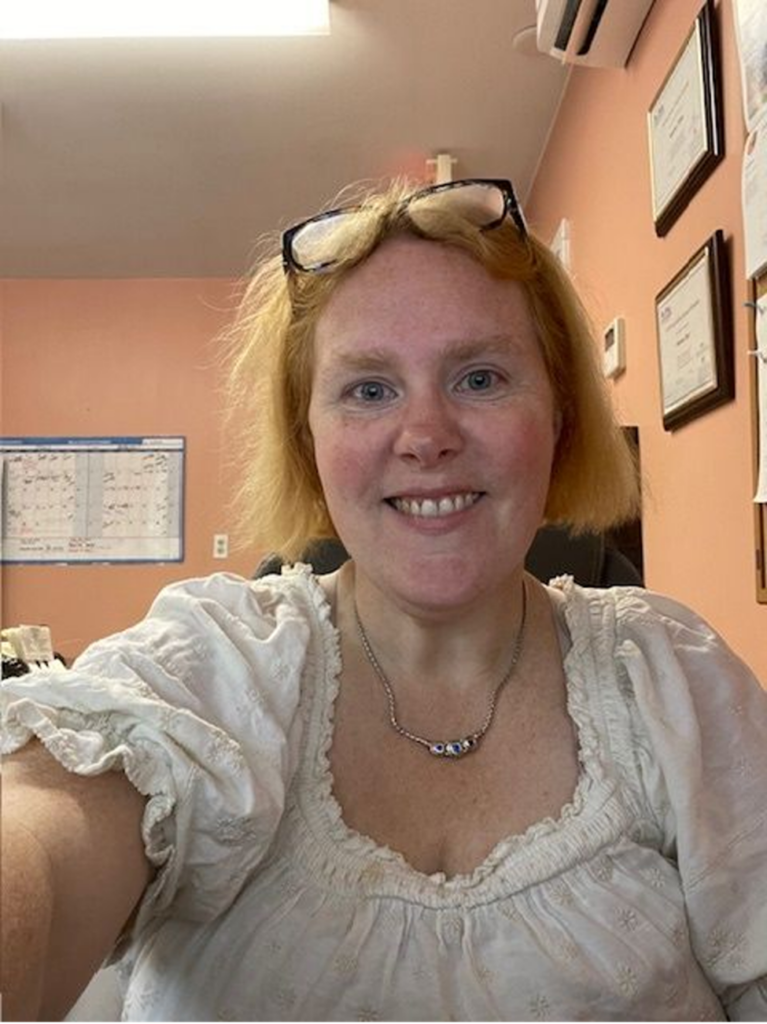 A smiling woman with reddish hair and glasses perched on top of her head.