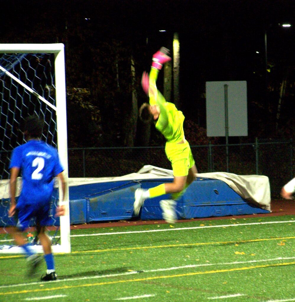 A young man in bright yellow gear leaps into the air with his hands above his head. the goalpost is in the background.
