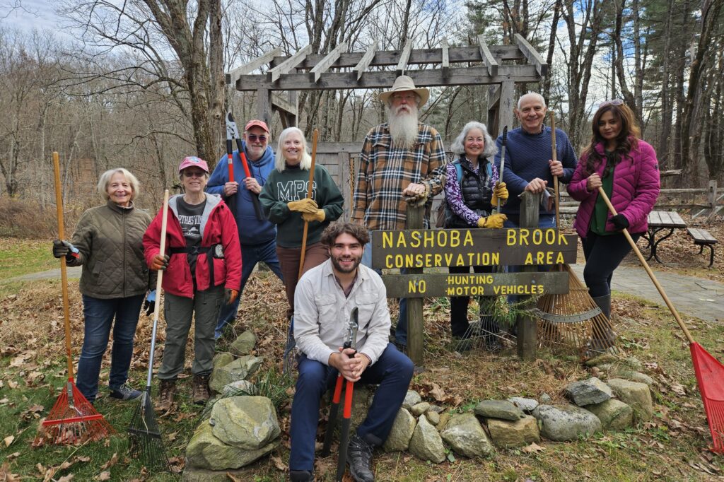 Some of the same volunteers pose with tools at the entrance to the Nashoba Brook Conservation Area.