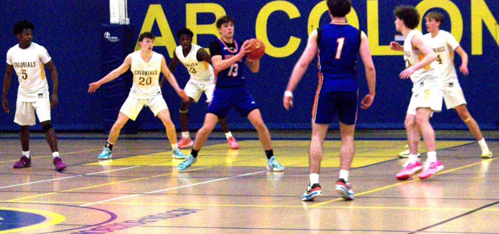 A boy in a blue uniform holds the ball. He is surrounded by boys in white.