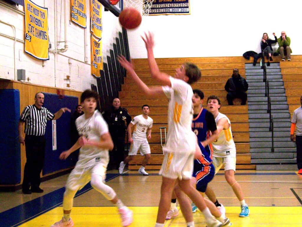 A boy shoots a basket while other players watch.