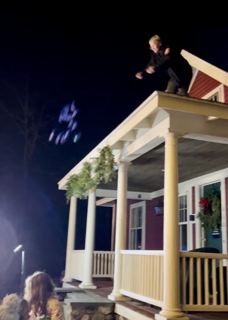 A woman stands on the porch roof of the Red House. She is throwing treat bags into the crowd.
