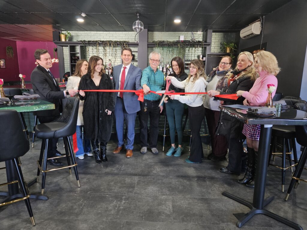 A group of people lined up with a red ribbon and oversized scissors.
