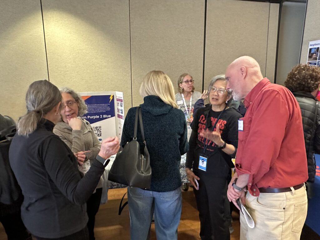 A group of people are standing in front of a table. Some people are talking, some might be listening.