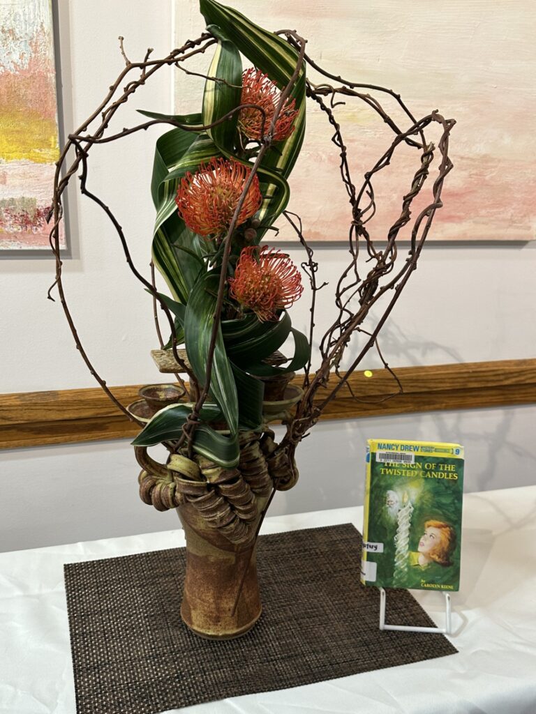 A tall display of twisted branches, long green leaves, and orange flowers in a handbuild clay vase.