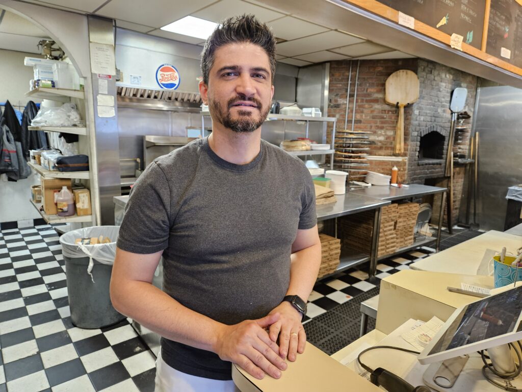 A man in a grey t-shirt stands at a counter in front of a commercial kitchen.