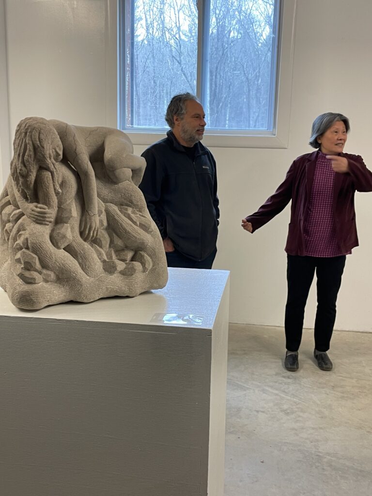 A man and a woman stand behind a small (about 2 feet high) granite sculpure of a woman draped over something that looks like branches. There are also gems (the treasure) carved in between the branches.