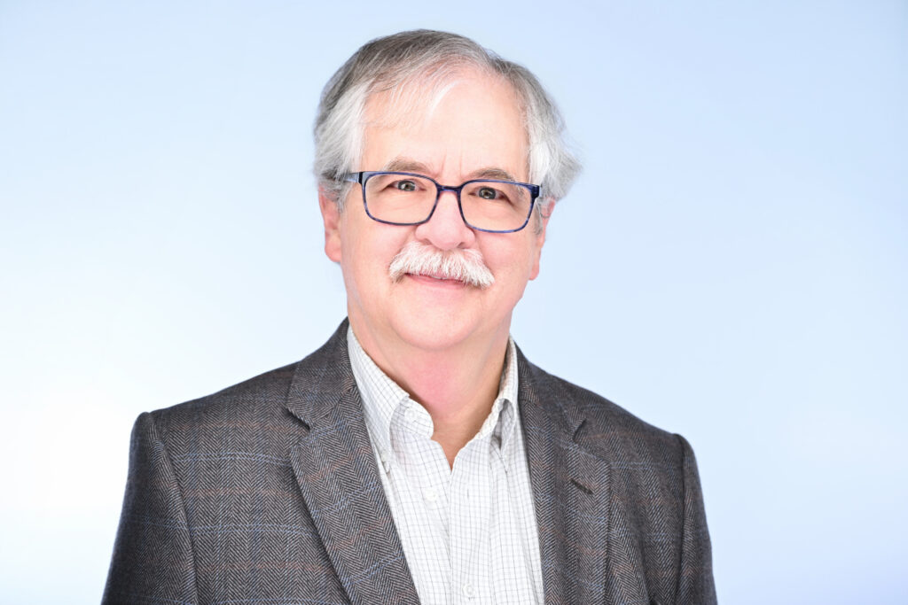 An gray-haired man with glasses and a sport coat.