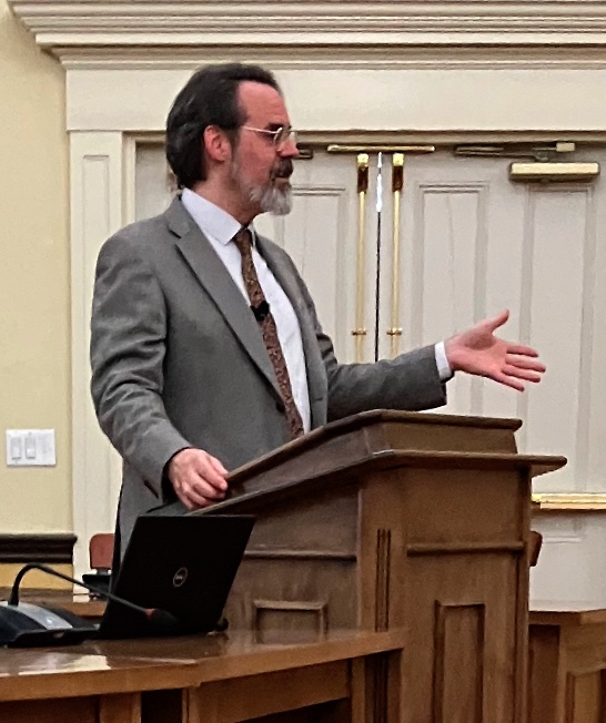 A bearded man in a suit stands at a podium.